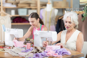 Elderly and adult women seamstresses sewing on machine in sewing workshop