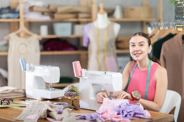 Adult female seamstress sewing clothes on sewing machine in workshop