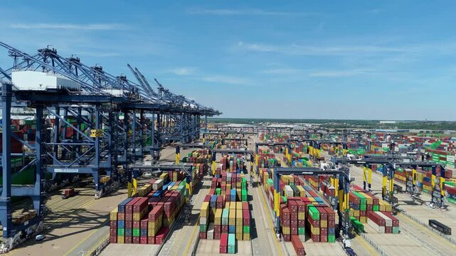 Aerial drone shot Felixstowe busy port cargo ships, shipping containers, huge cranes, loading and unloading heavy goods vehicles summer maritime business England UK
