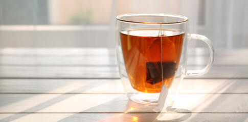 Cup of hot tea on white wooden table near window