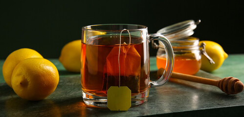 Cup of hot tea, lemons and honey on table against dark background, closeup