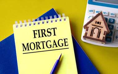 FIRST MORTGAGE - words in a yellow notepad with a calculator and a wooden house in the background