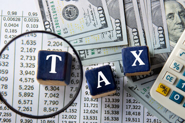 TAX - word on wooden cubes against the background of banknotes and calculator