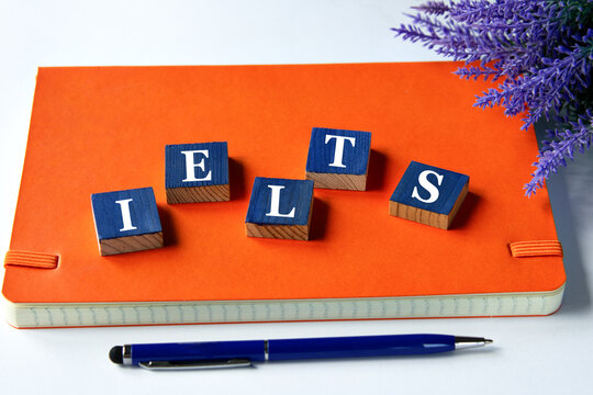 IELTS - a word written on wooden cubes on an orange notepad with a pen lying nearby