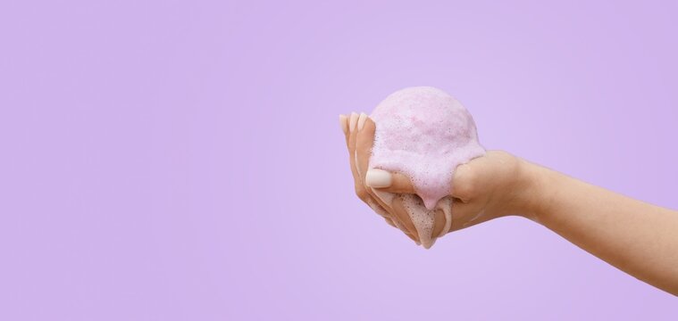 Hand holding dissolving bath bomb on lilac background with space for text