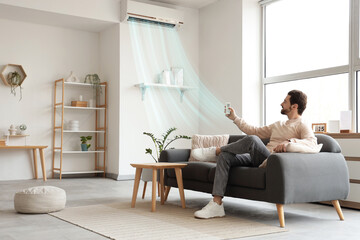 Young man turning on air conditioner from sofa at home