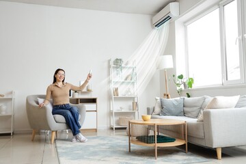 Young woman switching on air conditioner in living room