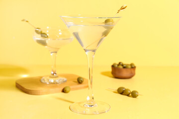 Glasses of martini with olives on yellow background