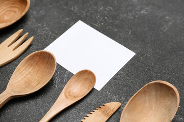 Composition with blank card and wooden cutlery on dark background, closeup
