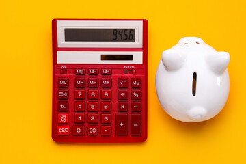 Red calculator and piggy bank on orange background