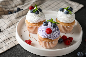 Plate of delicious cupcakes with blueberries, raspberries and mint on black background