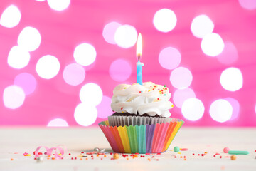 Tasty Birthday cupcake with burning candle on table against blurred lights