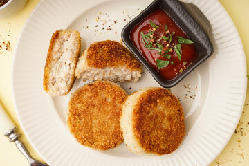 Plate with tasty meat cutlets and sauce on yellow background