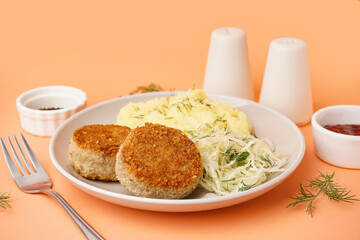 Plate of tasty meat cutlets with mashed potatoes and salad on orange background