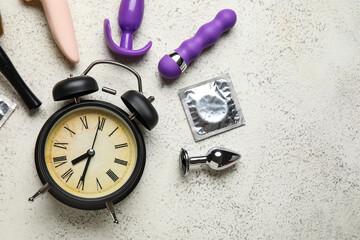 Alarm clock with different toys and condom on grunge white background. Time for sex