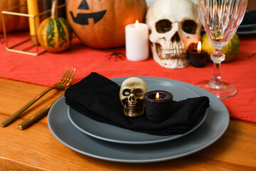 Festive table setting for Halloween celebration with skulls and burning candles, closeup