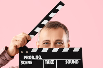 Mature actor with movie clapper on pink background, closeup