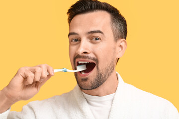 Handsome man brushing teeth on yellow background, closeup