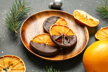 Wooden plate with chocolate dipped dried orange slices and fir branches on black background