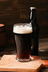 Glass and bottle of cold dark beer on table against wooden background
