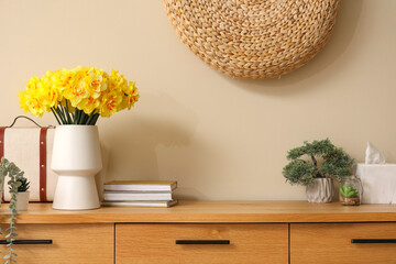 Vase with beautiful daffodil flowers on chest of drawers