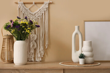Vase with wild flowers, frame, lamp and decor on chest of drawers in room