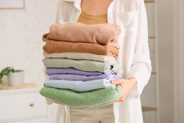 Young woman with stack of stylish clothes at home, closeup