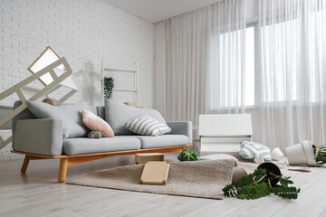 Interior of messy living room with sofa and overturned things after earthquake
