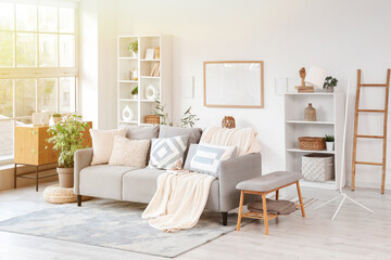 Interior of light living room with grey couch, shelf units and frames