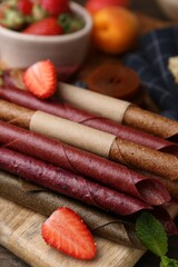 Tasty candied leather rolls, fruits and berries on wooden table, closeup
