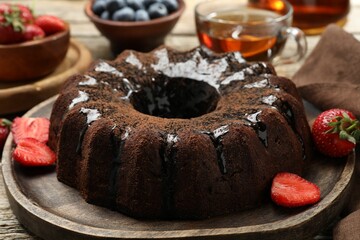 Tasty chocolate bundt cake with glaze, tea and berries on wooden table, closeup