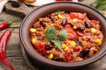 Tasty chili con carne in bowl on wooden table, closeup