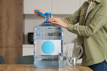Woman opening bottle of clean water on table in kitchen