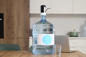 Bottle of clean water with glass and laptop on table in kitchen