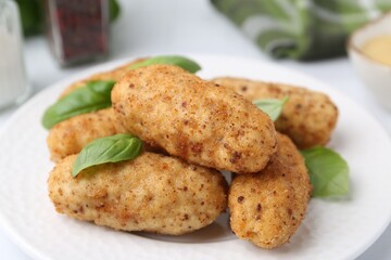 Tasty fried croquettes and basil on white table, closeup