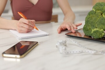 Woman developing diet plan at white marble table indoors, closeup