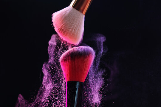 Makeup brushes with colorful eye shadows on black background, closeup