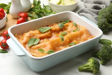 Tasty vegetarian lasagna in baking dish and ingredients on white table, closeup