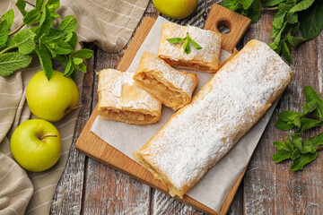 Tasty apple strudels with powdered sugar, mint and fruits on wooden table, flat lay