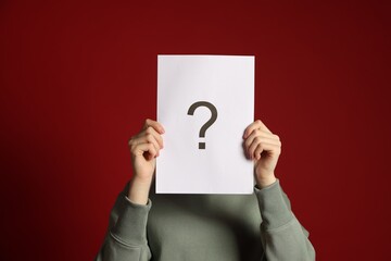 Anonymity. Woman hiding behind paper sheet with question mark on dark red background