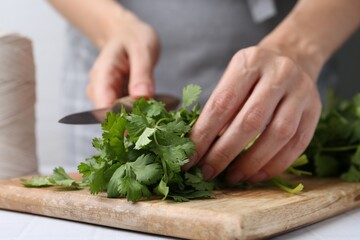 Woman cutting fresh cilantro at white table, closeup