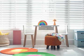 Small table, chairs, pouf and toy in stylish playroom. Interior design