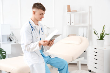 Male medical intern with clipboard sitting on couch in clinic