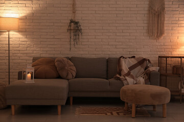 Interior of dark living room with pouf, sofa and glowing lamp near white brick wall