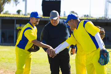 Baseball coach and male players huddling before starting game on grass field by dugout with gloves