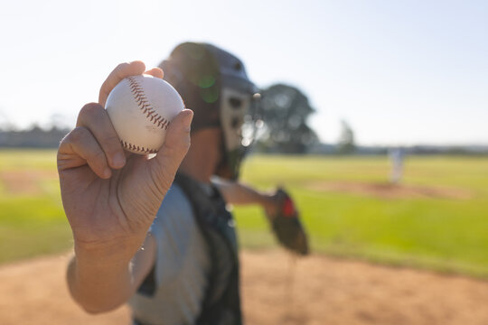 male catcher wearing mask crouching behind home plate on sunlit baseball diamond gripping baseball