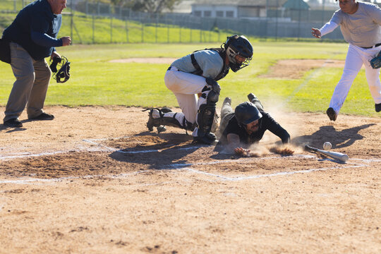 Male baseball players and umpire sliding and tagging at home plate with catcher's mitt and baseball