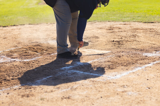 Male umpire crouching over home plate brushing chalk lines on sunlit dirt infield
