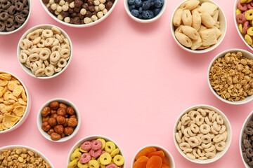 Frame made of bowls with different tasty cereals, dry fruits and nuts on pink background