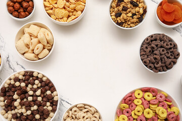 Frame made of bowls with different tasty cereals, dry fruits and nuts on grunge white background